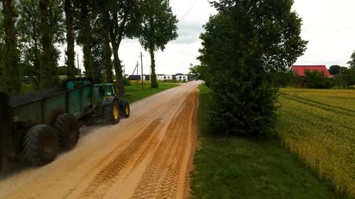 shot of tractor driving on a dirt road with trees and bright sky
