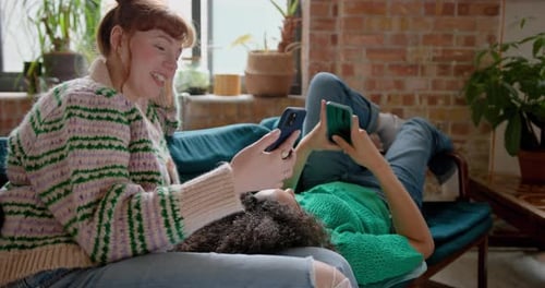 Two Young adult Female Friends looking at a Smartphone Together in a shared loft apartment on Sofa