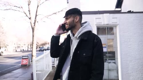 Smiling young man talks on smart phone in sunny urban city lifestyle