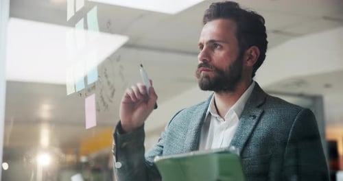 Focused Businessman Writing on Glass Whiteboard in Office