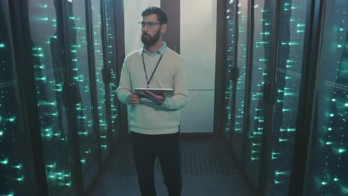 Man in Server Room Holds Tablet and Inspects