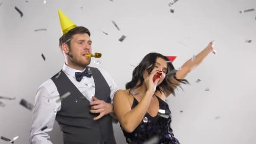 Festive couple celebrating with party horns and confetti