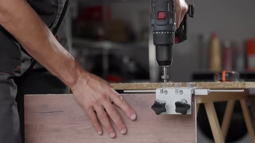 Man Using Drill on Wood in Workshop