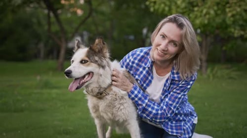 Woman Pets Her Dog in a Grassy Yard