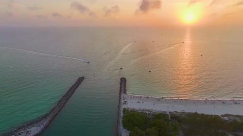 Sunset Seascape of Rock Jetty Barrier and Boats Sailing at Harbor on Colorful Ocean Water Near