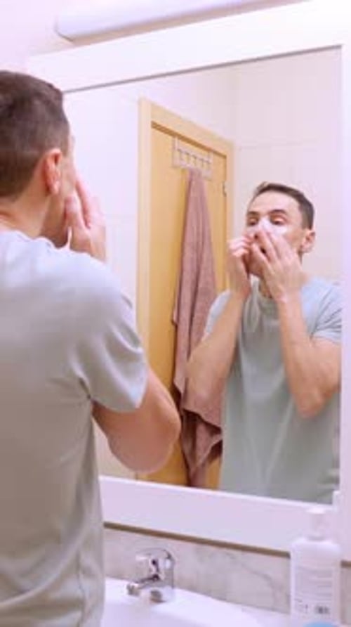 Man Applying Eye Patches in Bathroom Mirror