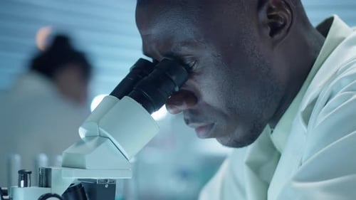 Focused Scientist Analyzing Sample Through Microscope in Lab