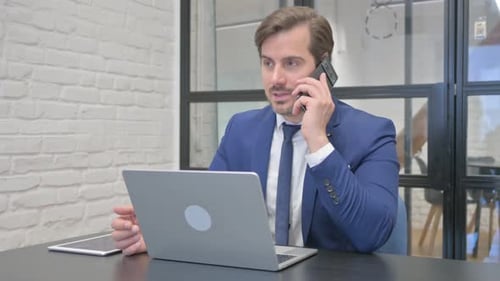 Man in Suit Talks on Phone at Office Desk