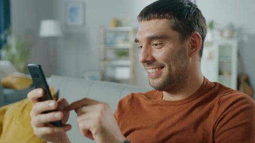 Smiling Man Using a Mobile Phone on Couch Indoors