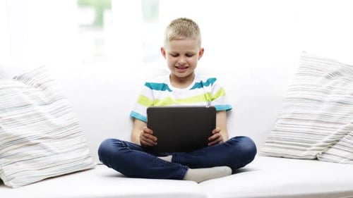 Boy Sitting Cross-Legged Using Tablet on White Couch