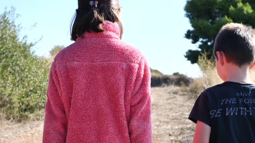 Brother and sister walking together on a path. Slow-motion gimbal shot.