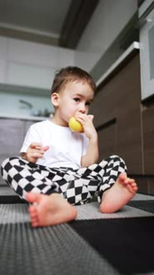 Child Eating Yellow Fruit Sitting on Kitchen Floor
