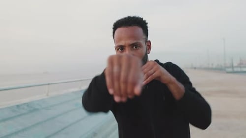 Young athlete boxer practicing punching technique while standing on the embankment
