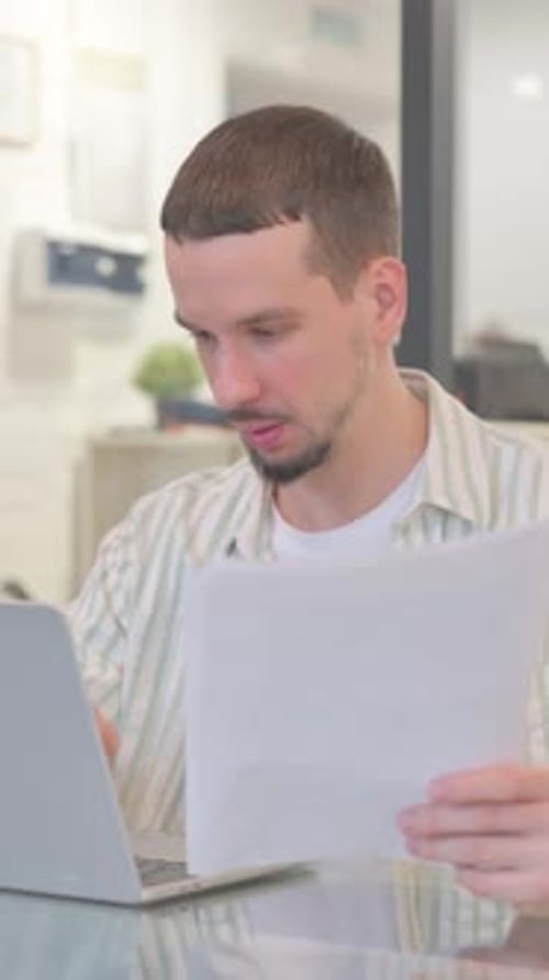 Man reviewing documents and laptop in bright home office