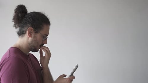 Man Looks at Smartphone with Hand on Chin