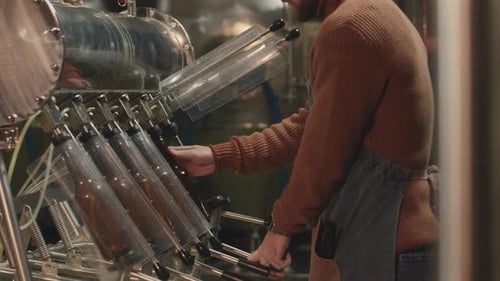 Worker Filling Glass Bottles on Machine in Factory