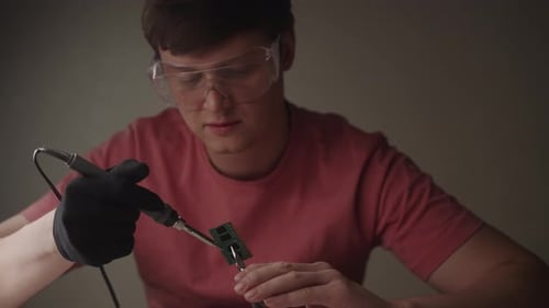 Porträt eines erfahrenen Technikers mit Schutzbrille und Handschuhen, der komplizierte Lötarbeiten durchführt
