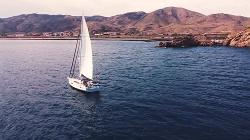 Sailboat sailing by coastline seashore against sunset and mountains. Sail boat in the south coast of