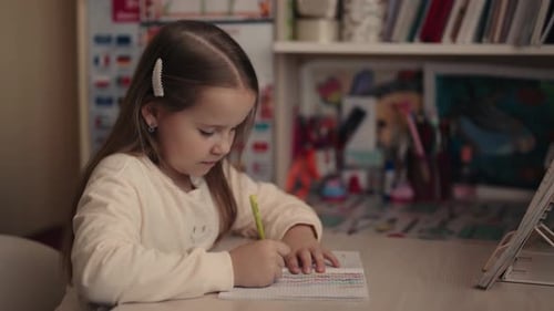 Girl Draws in Notebook at Desk Indoors