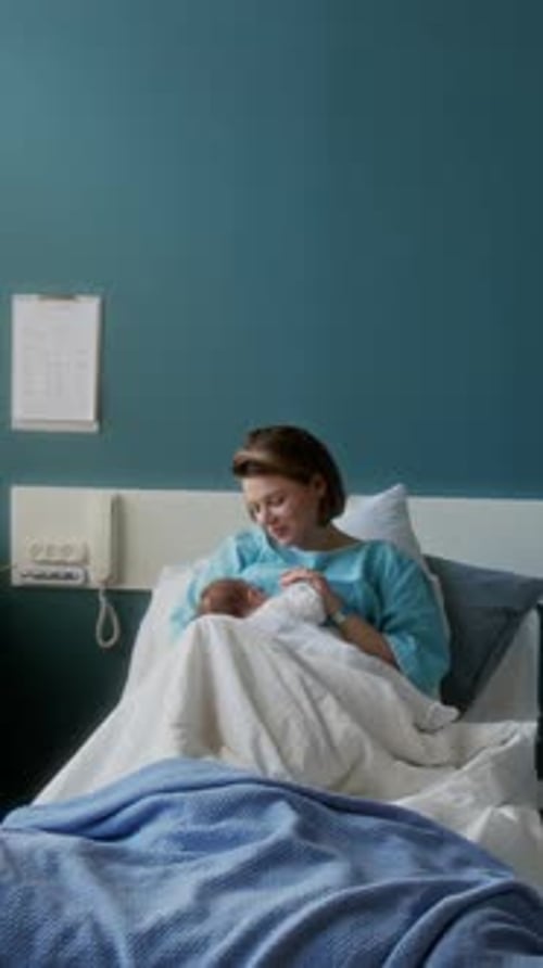 New Mother Cradles Newborn Infant in Hospital Bed