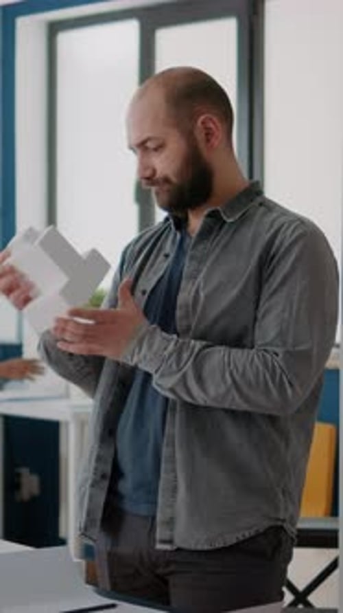 Ingeniero de Vídeo vertical diseñando planos de construcción con un modelo de construcción en la oficina