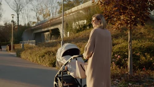 Young mother strolls through park with stroller as the sun sets beautifully