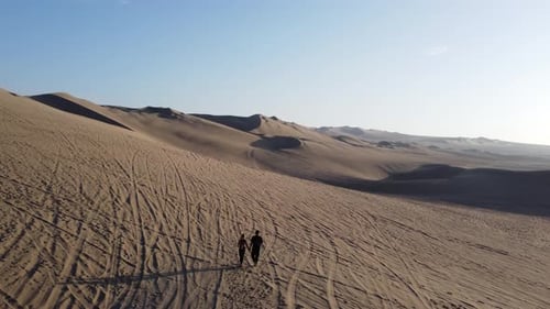 The travelers walk through the desert to meet the buggy car. Huacachina, Peru