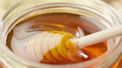 Honey Dipper Stirring Honey in Jar Close Up
