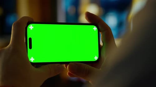 Person Holding Smartphone with Bright Green Chroma Key Screen in Cozy Indoor Setting Showcasing