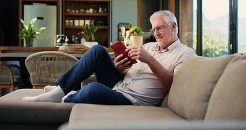 Reading book, happy and senior man on sofa with literature, story and literacy in home