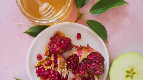 Comida tradicional para la festividad del Año Nuevo judío de Rosh Hashaná con miel, granada y manzanas sobre fondo rosa