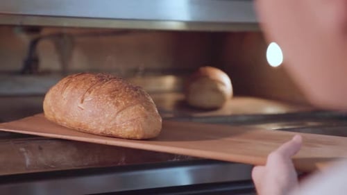 Baker takes freshly baked bread loaf out of the oven with peel in slow motion