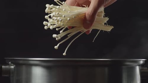 Hand Adding Enoki Mushrooms to Steaming Pot