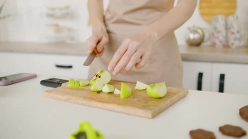 Close Up Shot in a Lit Kitchen a Skilled Person Slices Fresh Green Apples on a Rustic Cutting Board