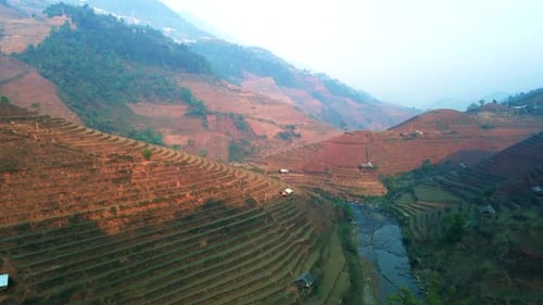 Rice terrace drone fly through valley with stream as early morning sun illuminates the north Vietnam