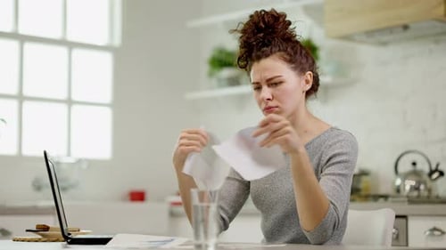A Frustrated Woman Analyzing a Report at Her Home Office Workspace Amidst Distractions