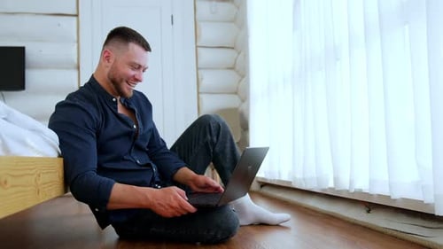 Man Sitting on Floor Using Laptop in Bedroom