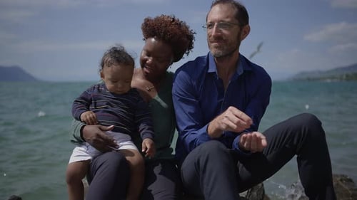 Family Sits By Lake Throwing Rocks