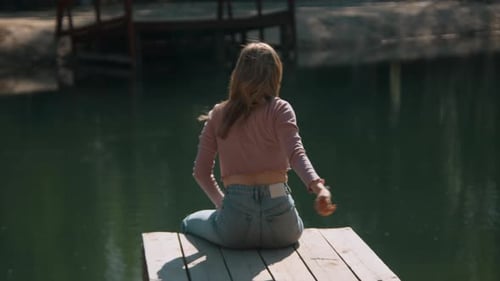 Attractive young woman sits on pier and throws stones.