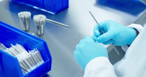 Over-the-should shot of lab technician in lab jacket and blue medical gloves tamps and twists cannab