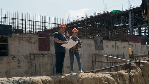 Construction manager and engineer discussing and checking plans on construction site.