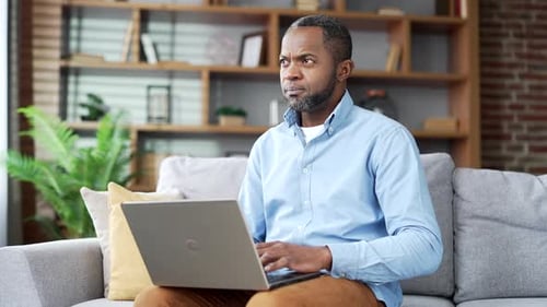 Confident mature african american man typing on laptop sitting on sofa in living room at home office