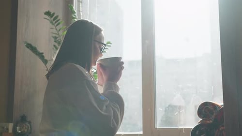 Woman Enjoys Coffee Near Window with Sunlight and City View
