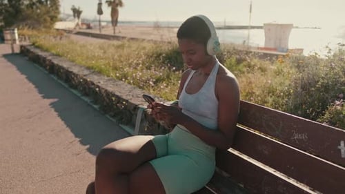 Woman Uses Smartphone on Bench Near Beach