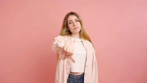 Woman Gives Thumbs Down on Pink Background