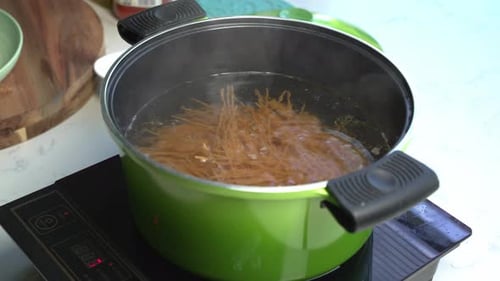Mixing with a wooden spoon spaghetti in hot boiling water in a pot, home cooking, close up