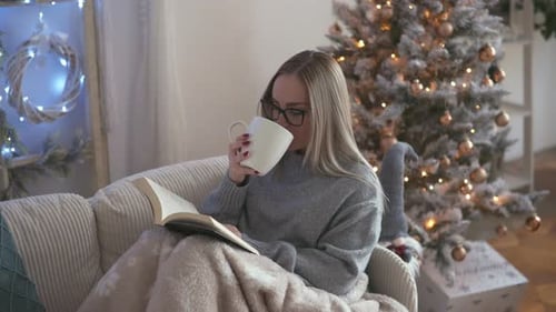 Woman Reading Book and Drinking Coffee by Christmas Tree