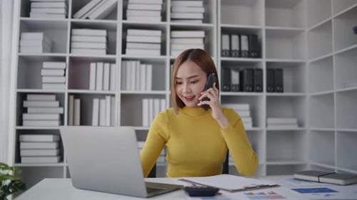 Businesswoman is talking to clients and colleague on the phone and working on laptop in office