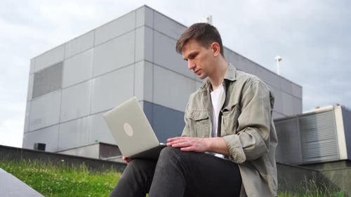 A young male student of Caucasian race works at the computer in the park. College.