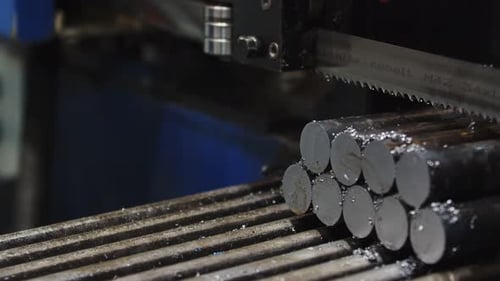 A Closeup of Metal Rods Automatically Moving on a Production Machine Under a Bandsaw at a Factory